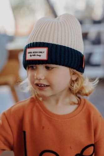 Menino loiro com gorro creme e azul-marinho e camisola laranja