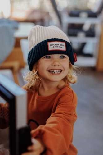 Menino a sorrir com gorro creme e azul-marinho, a brincar