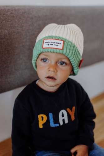 Bebé sentado com gorro creme e menta e camisola azul-marinho