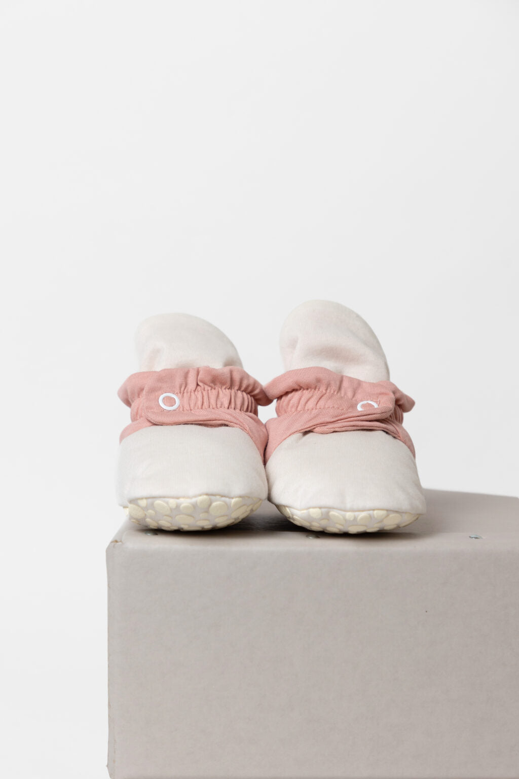 Botinhas de bebé creme e rosa vistas de trás em cima de um bloco