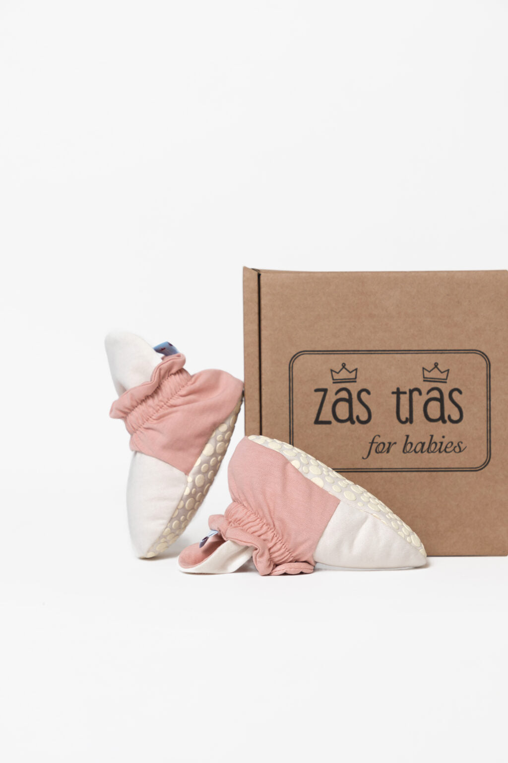 Botinhas de bebé creme e rosa ao lado da caixa de cartão
